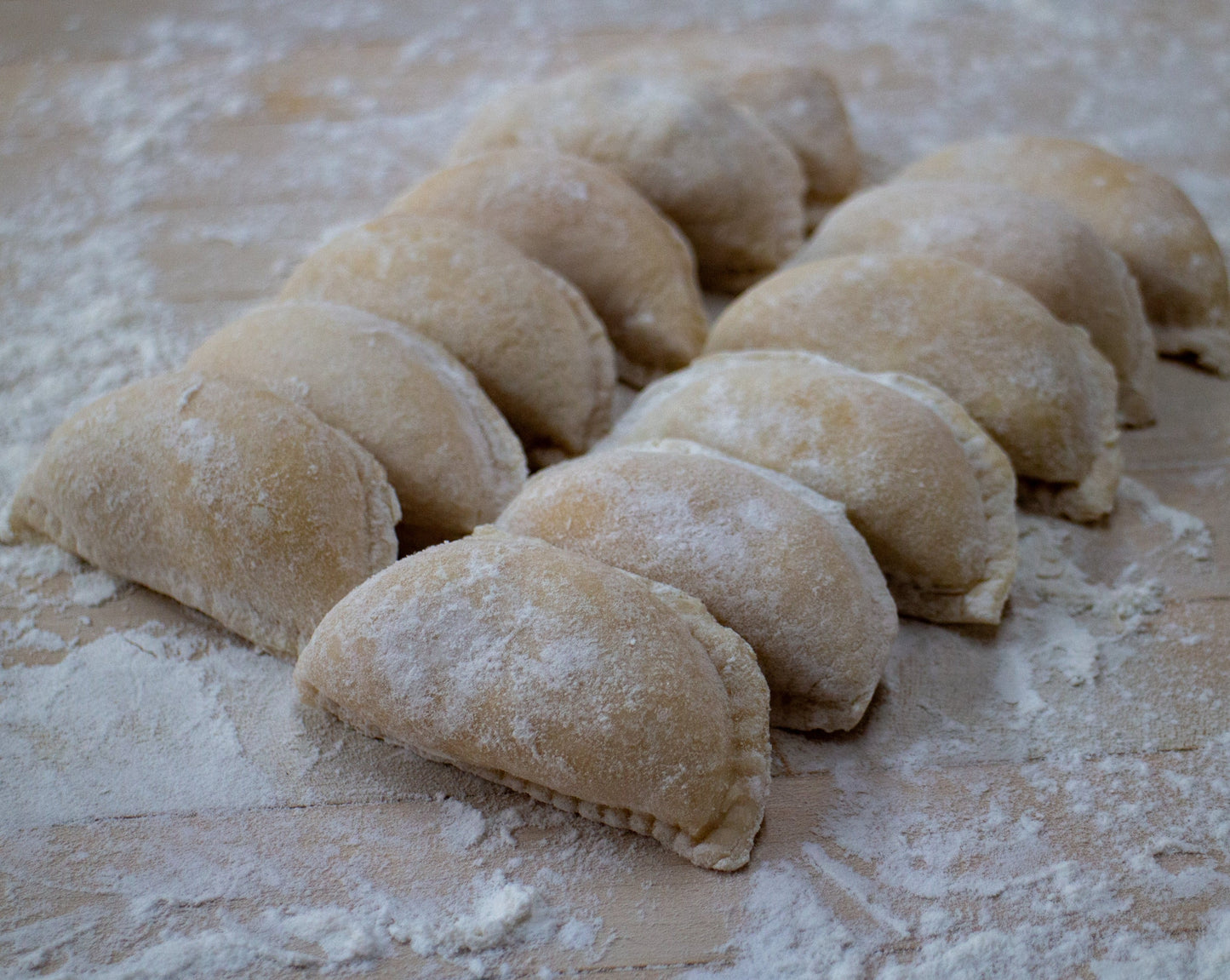 Two rows of six perogies sitting on a floured wooden table