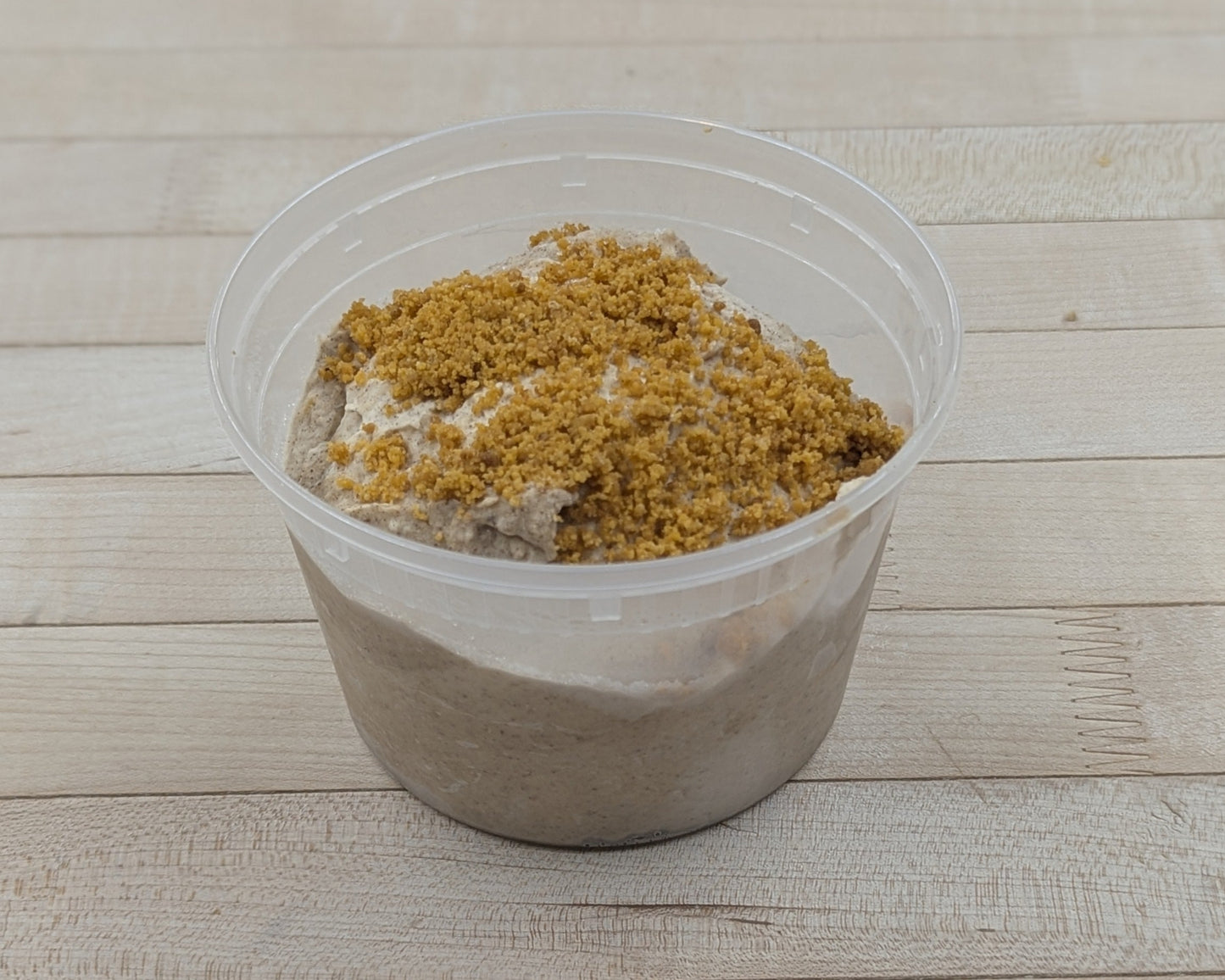 Clear plastic container with pumpkin spice cheesecake dip on a wooden surface