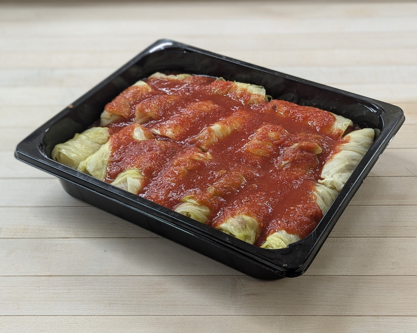 Plastic container with cabbage rolls in tomato sauce on a wooden surface
