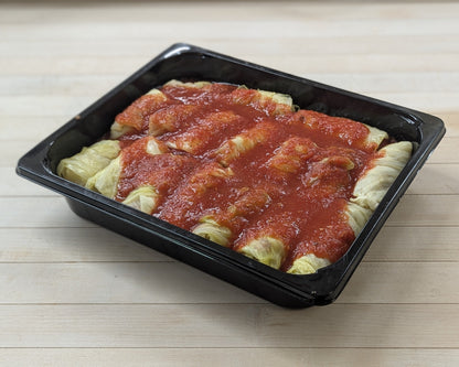 Plastic container with cabbage rolls in tomato sauce on a wooden surface