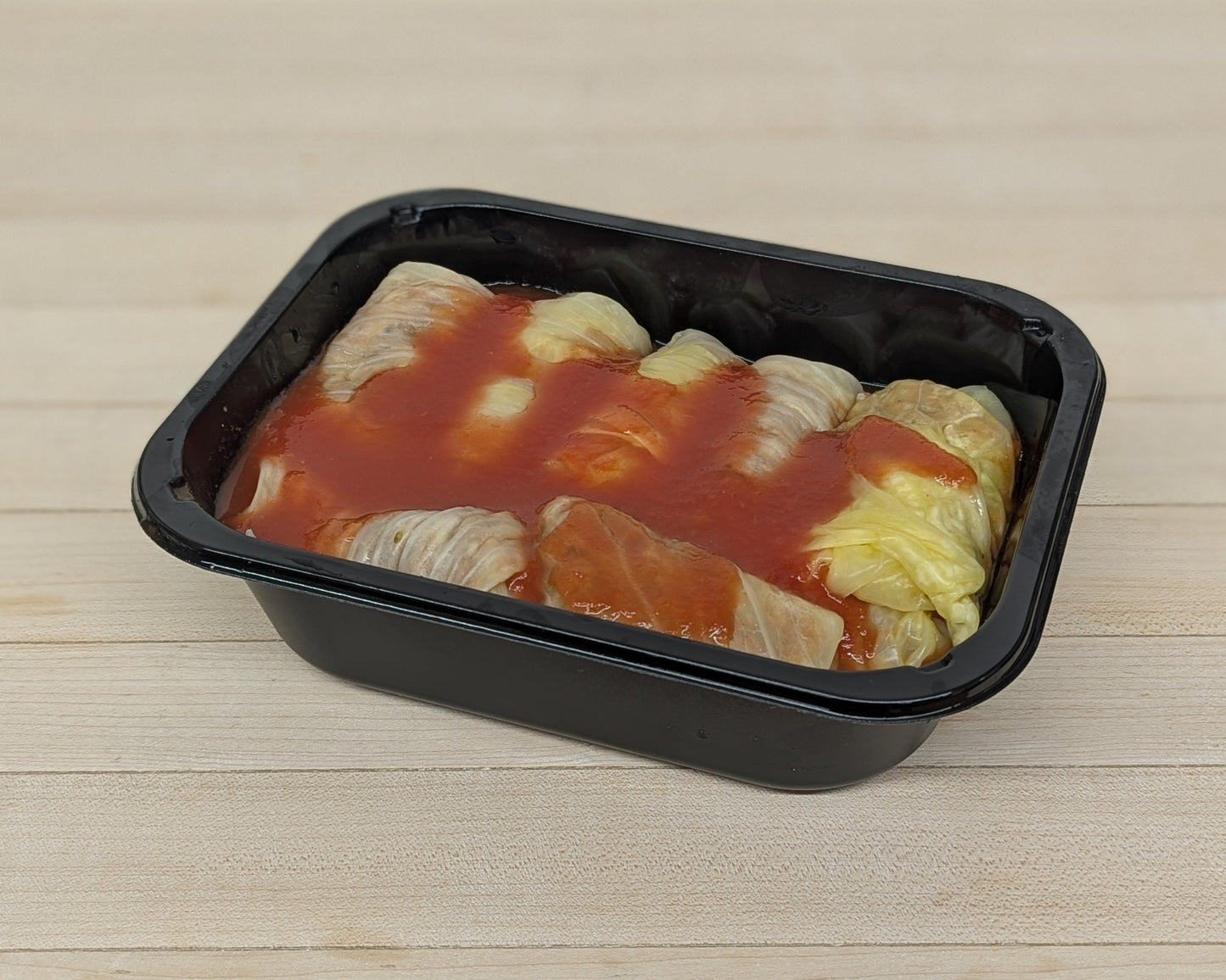 cabbage rolls with tomato sauce in a black plastic container on a wooden surface